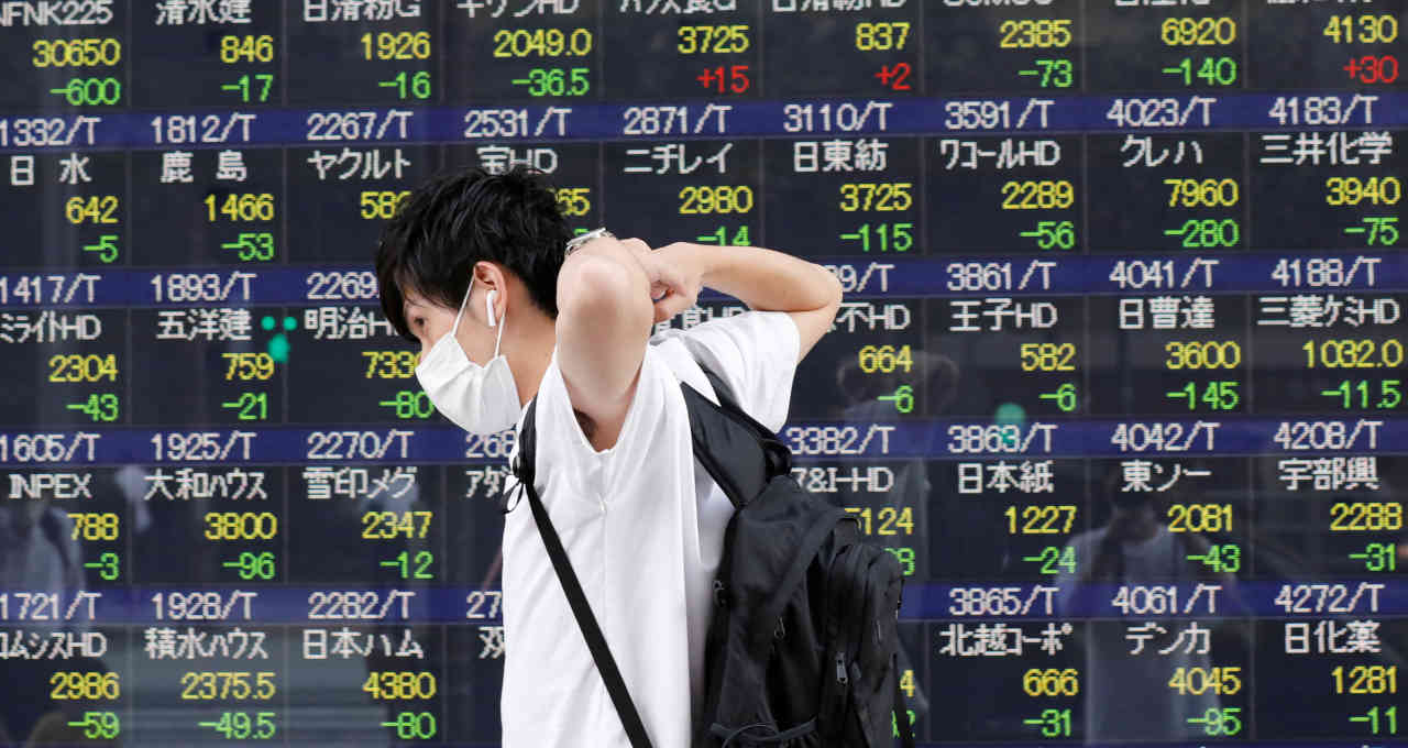 Homem passa por painel eletrônico com informações acionárias em uma corretora em Tóquio