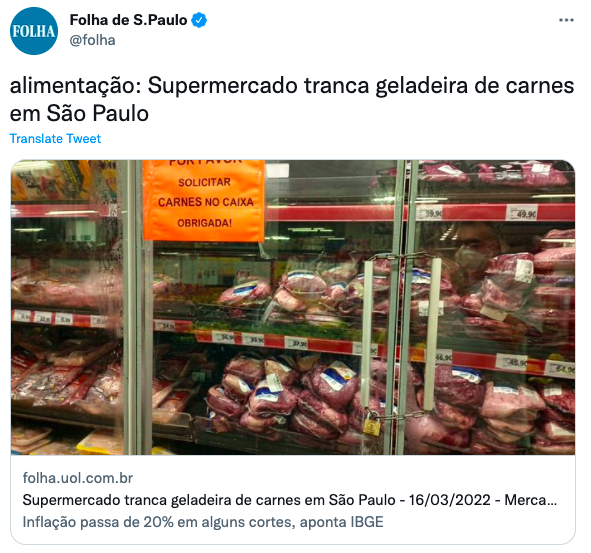 A foto mostra uma geladeira de carnes trancada, com a mensagem 'por favor solicitar carnes no caixa'.