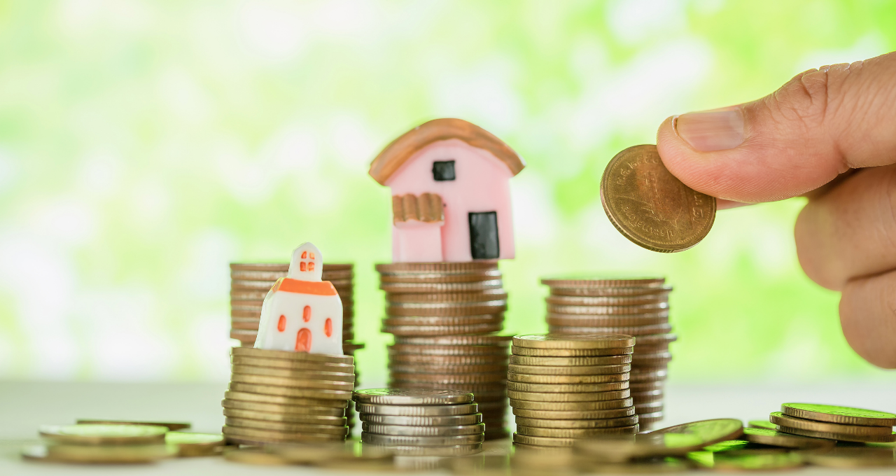 Miniaturas de casas empilhadas em cima de moedas, representando financiamento imobiliário