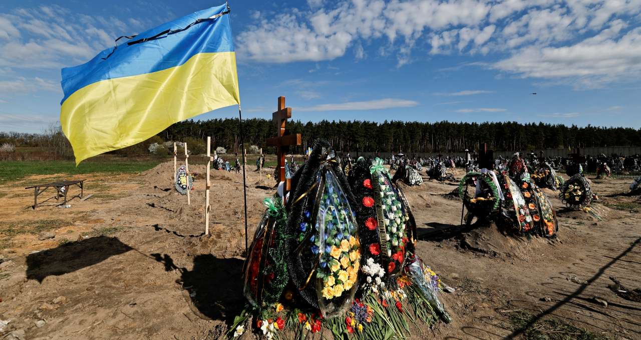 Bandeira da Ucrânia ao lado de covas de pessoas mortas durante invasão da Ucrânia pela Rússia