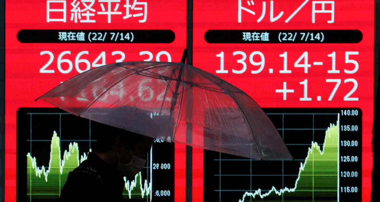 Homem de máscara em silhueta na frente de um monitor que mostra a taxa de câmbio do Iene e a taxa média de transações da Nikkei, em Tóquio, Japão