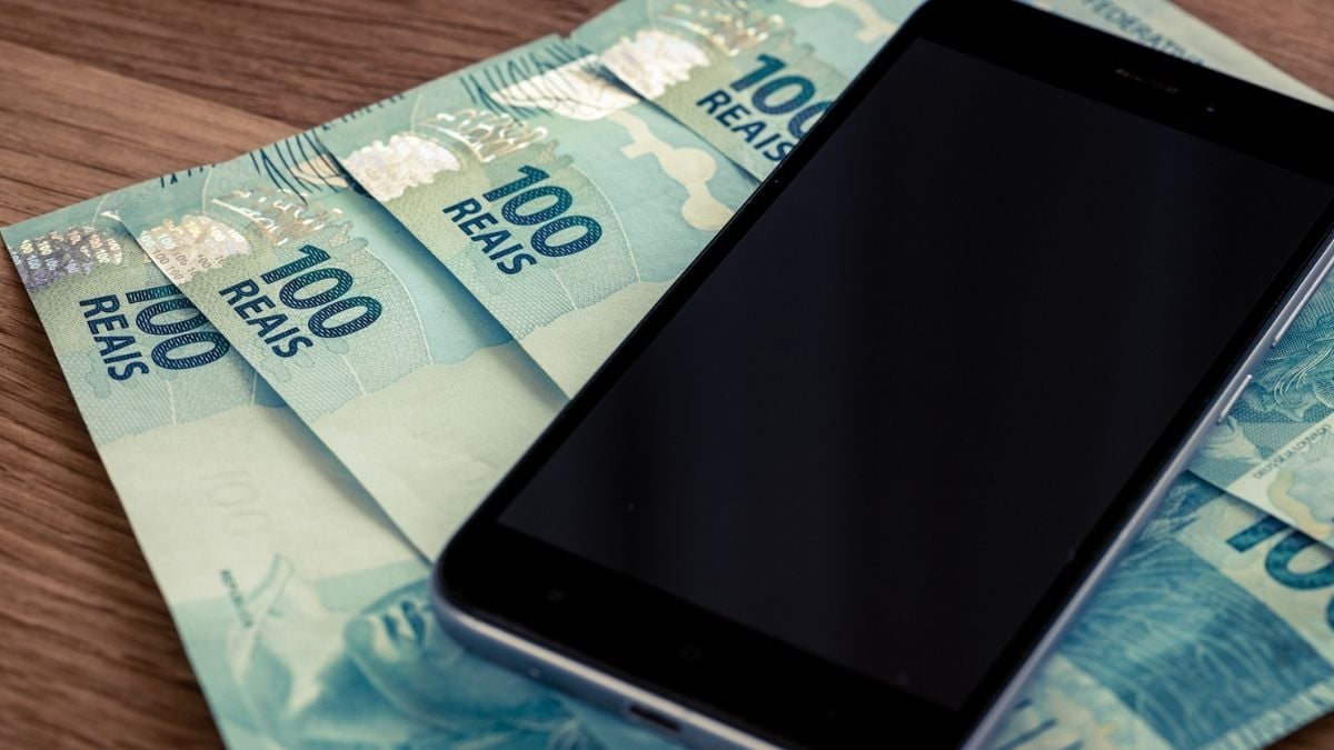 Smartphone em cima de notas de R$ 100 reais